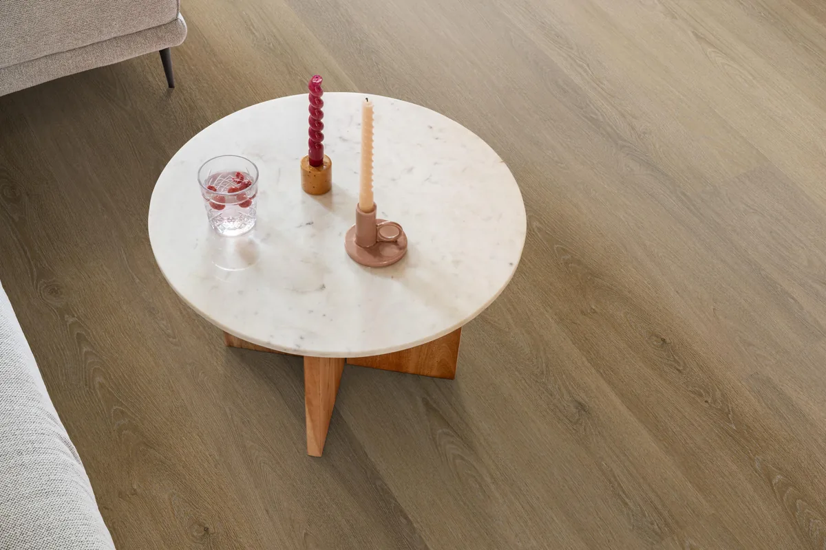 Sutton / Viranto Light brown, klik pvc in een woonkamer, met een ronde marmeren salontafel en twee kaarsen