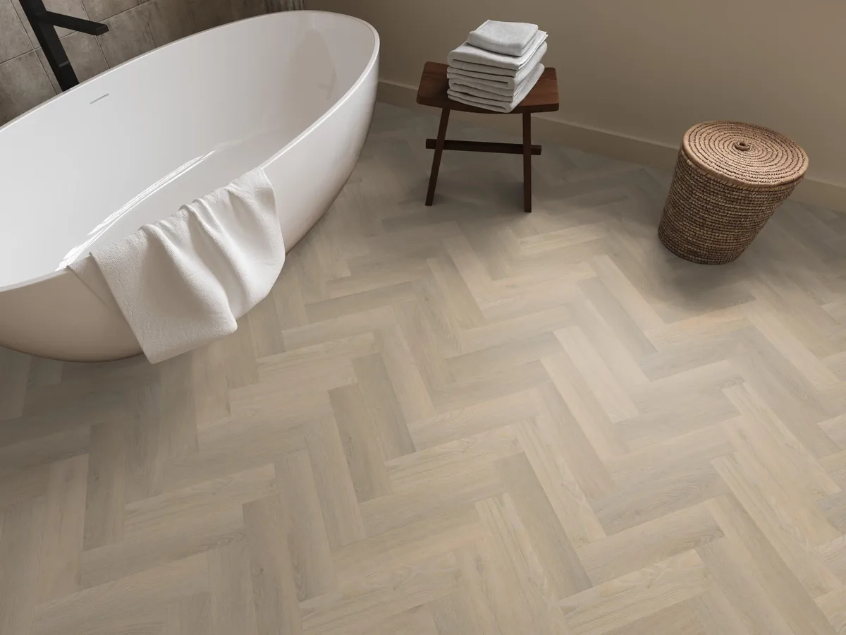 YUP / Spigato small beige, visgraat plak pvc in een badkamer, met een vrijstaand bad en een rieten wasmand