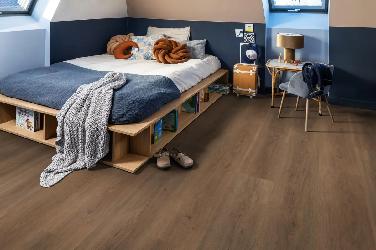 Parramatta / Robusto warm brown, plak pvc in een slaapkamer onder een schuin dak, met een houten bedombouw en sloffen ervoor