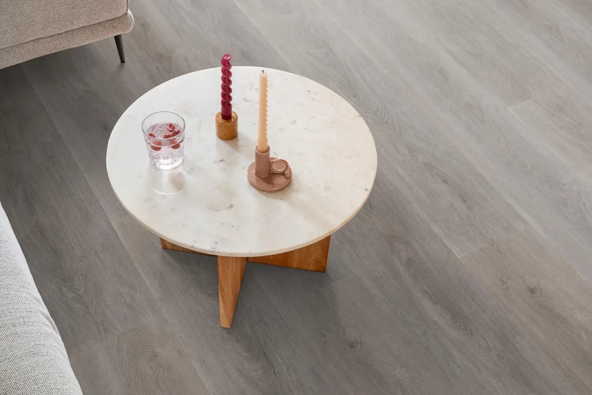 Parramatta / Robusto grey oak, plak pvc in een woonkamer, met een ronde marmeren salontafel en twee kaarsen