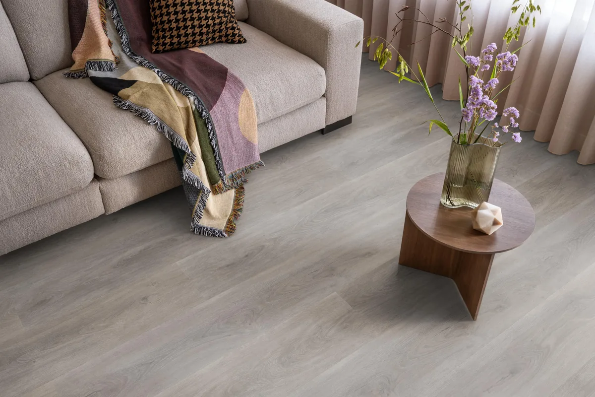 Parramatta / Robusto grey oak, plak pvc in een woonkamer, met een beige bank en een ronde bijzettafel met bloemen