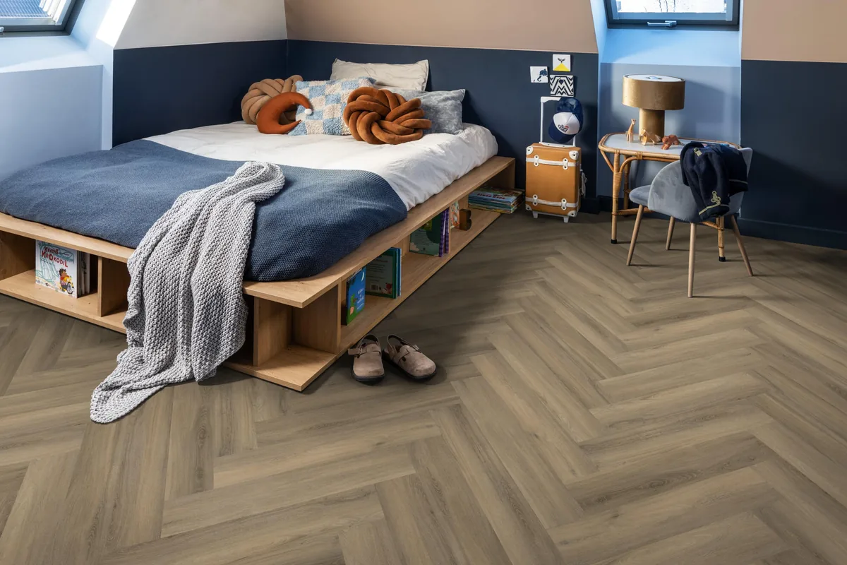 YUP / Spigato light brown, visgraat plak pvc in een slaapkamer onder een schuin dak, met een houten bedombouw en sloffen ervoor