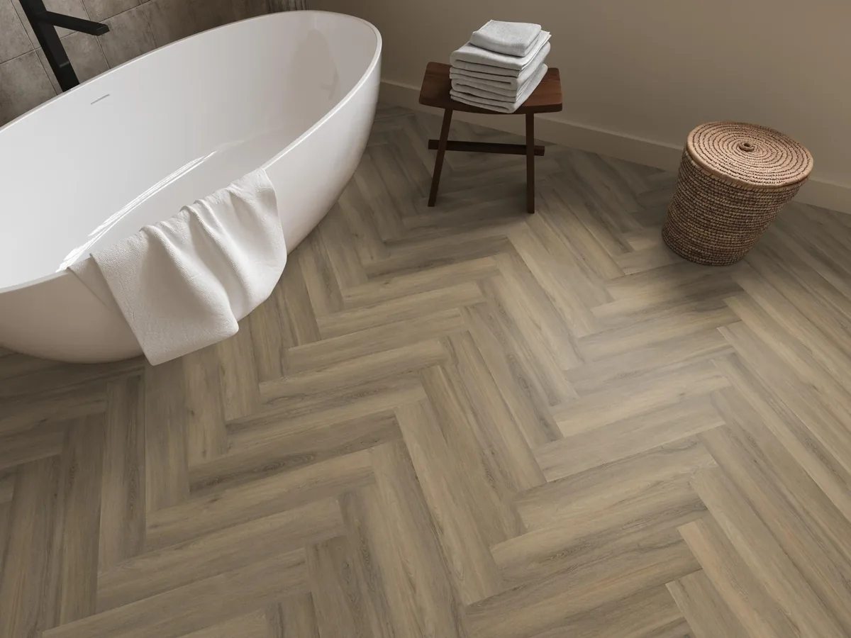 YUP / Spigato light brown, visgraat plak pvc in een badkamer, met een vrijstaand bad en een rieten wasmand