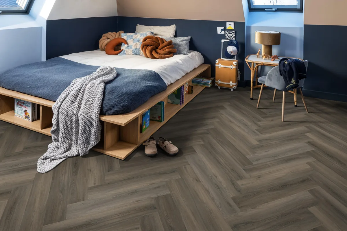 YUP / Spigato dark grey, visgraat plak pvc in een slaapkamer onder een schuin dak, met een houten bedombouw en sloffen ervoor