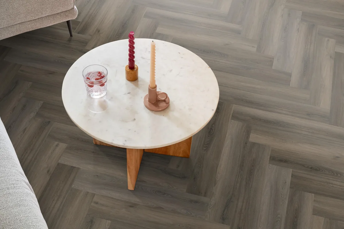 YUP / Spigato dark grey, visgraat plak pvc in een woonkamer, met een ronde marmeren salontafel en twee kaarsen