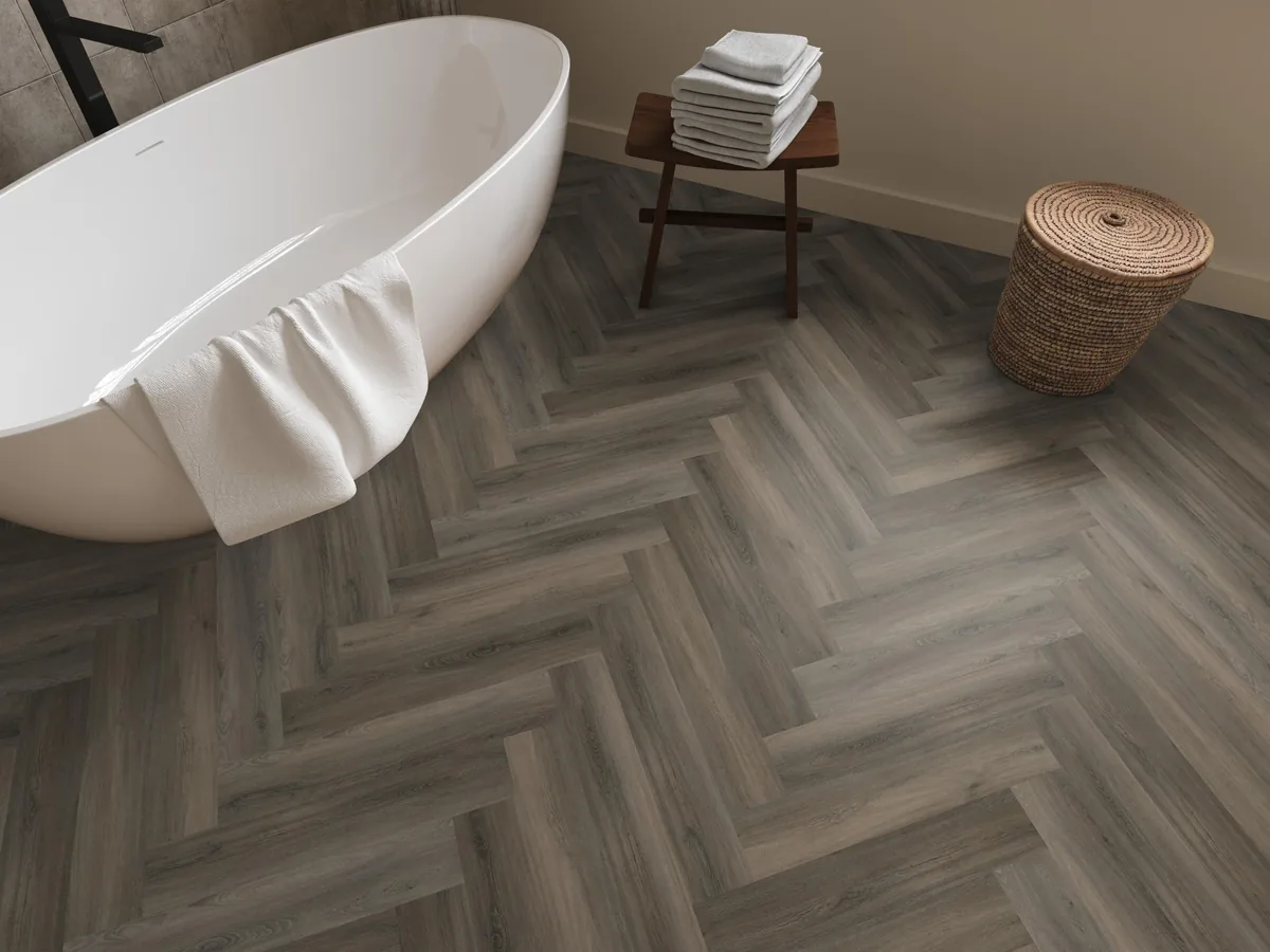 YUP / Spigato dark grey, visgraat plak pvc in een badkamer, met een vrijstaand bad en een rieten wasmand