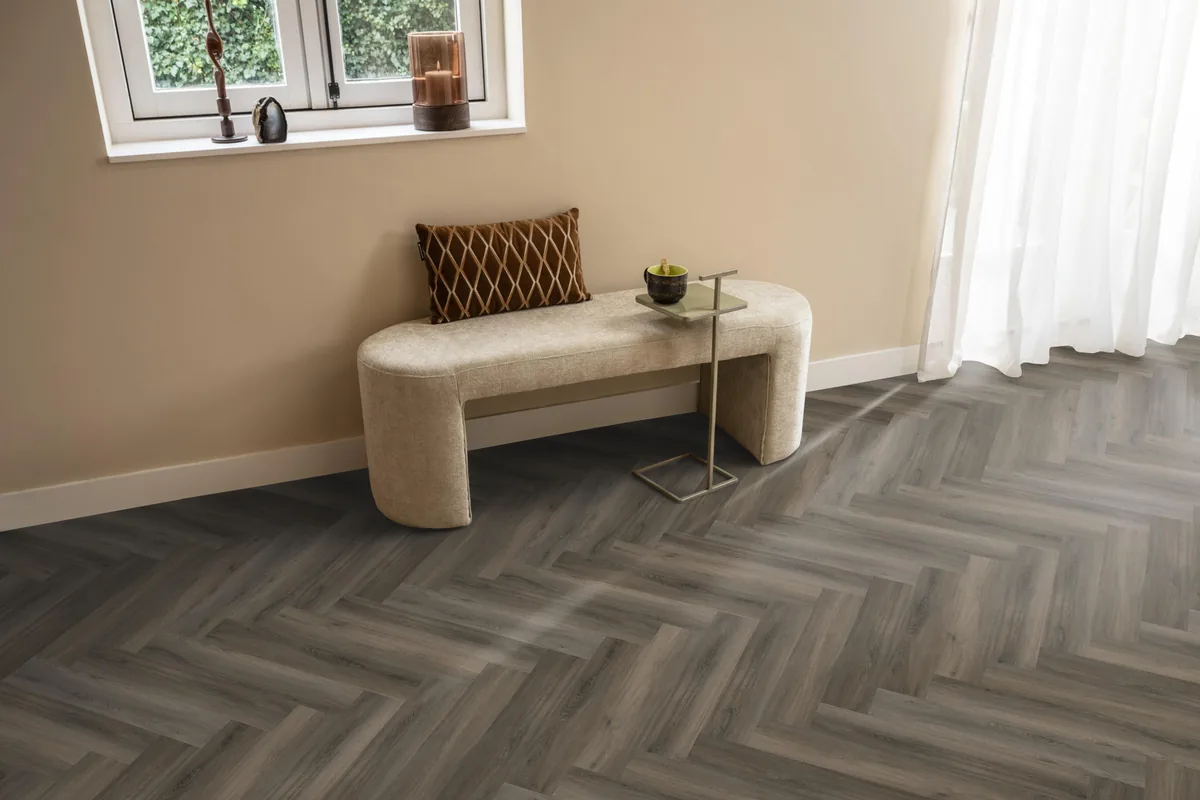 YUP / Spigato dark grey, visgraat plak pvc in een hal, met een bankje onder het raam en zonlicht over de vloer