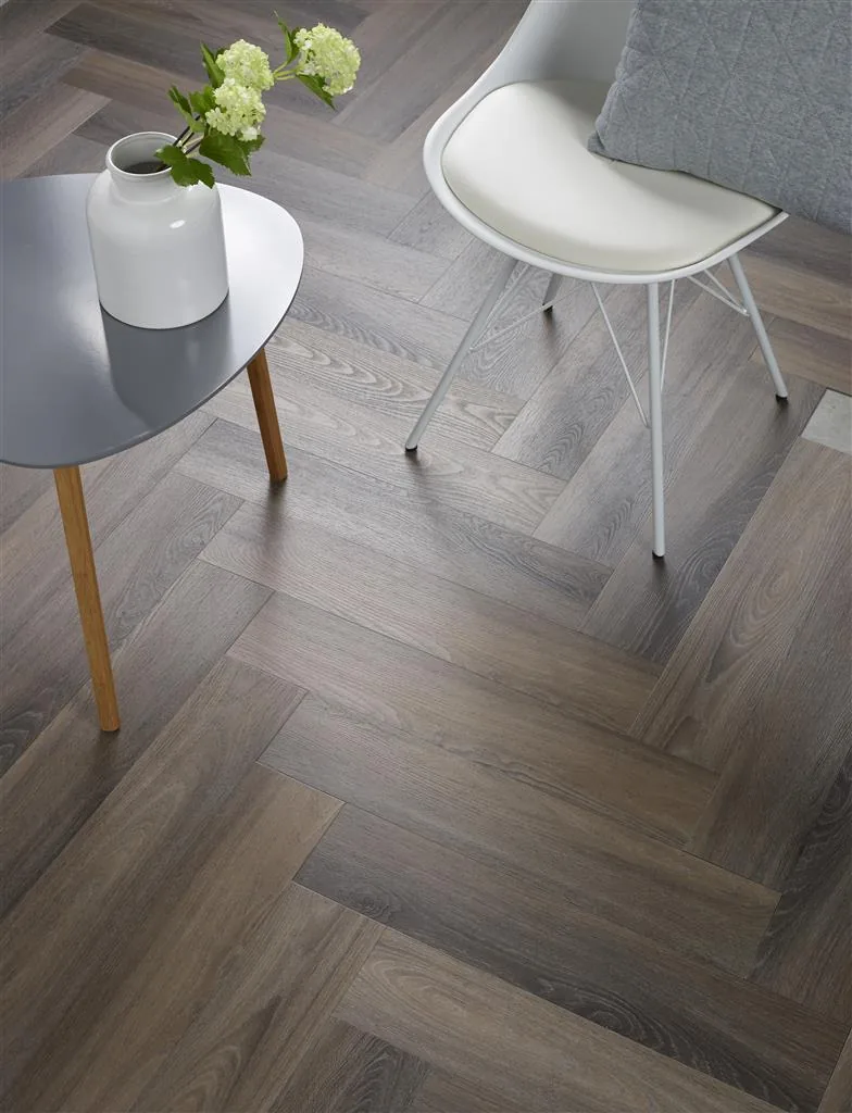 YUP / Spigato dark grey, visgraat plak pvc van dichtbij in een hoek, met een wit stoeltje en een koperen bijzettafel