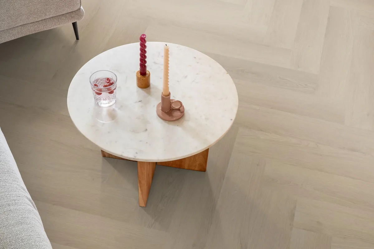 Merton / Navaro beige, visgraat plak pvc in een woonkamer, met een ronde marmeren salontafel en twee kaarsen