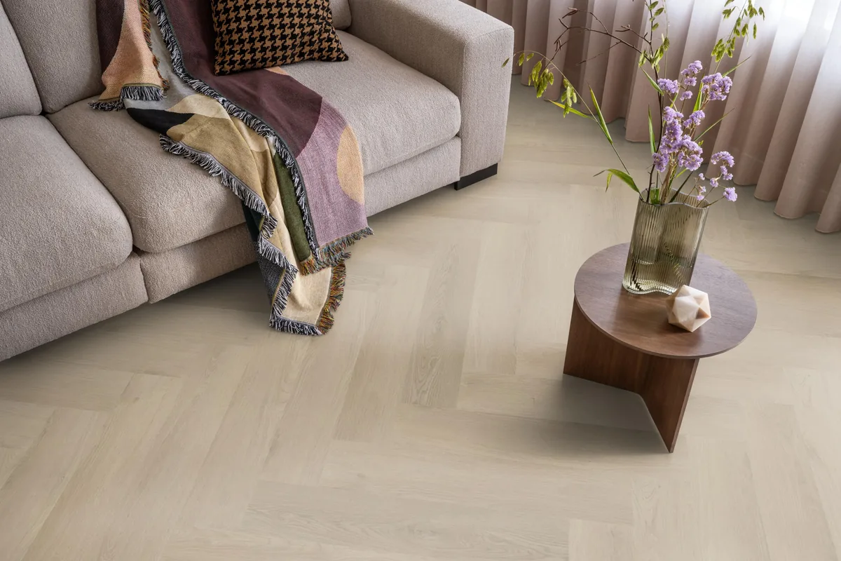 Merton / Navaro beige, visgraat plak pvc in een woonkamer, met een beige bank en een ronde bijzettafel met bloemen