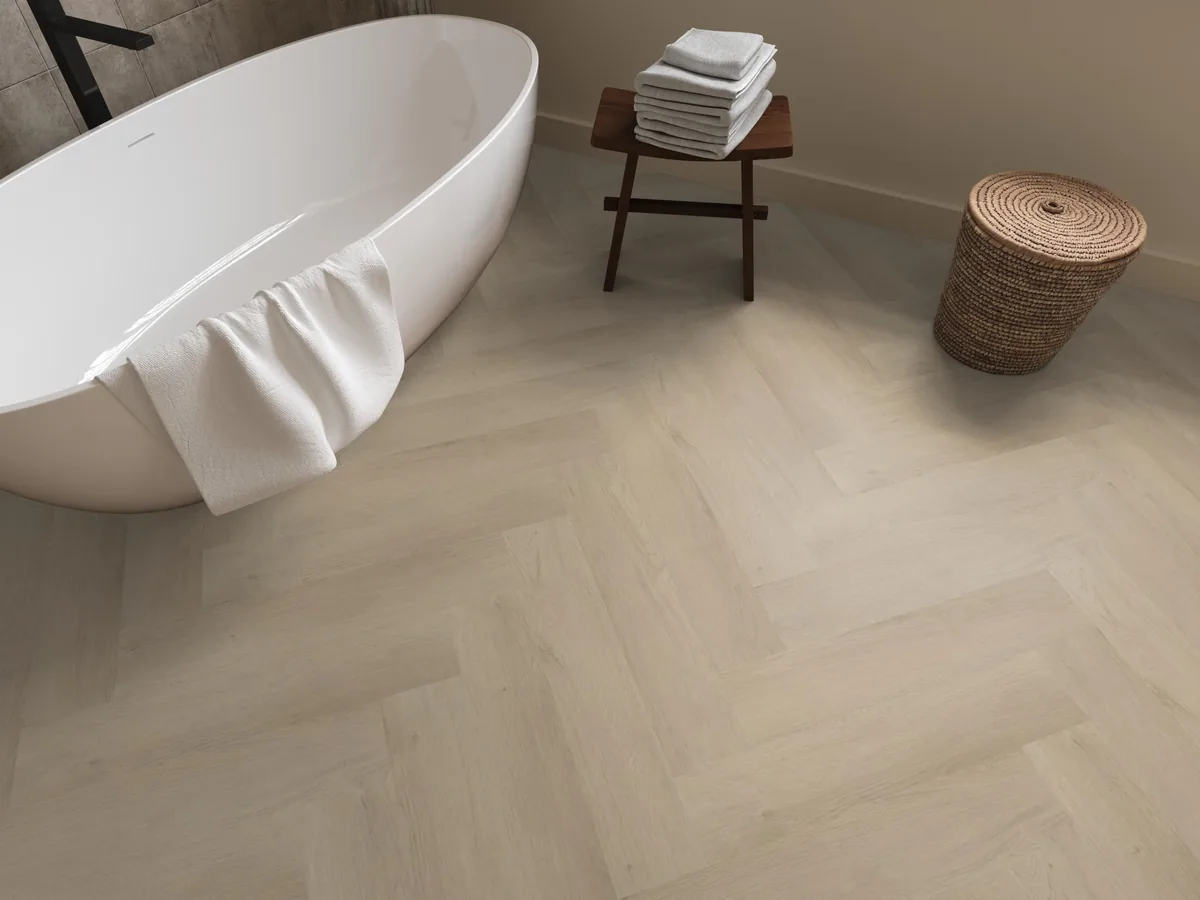 Merton / Navaro beige, visgraat plak pvc in een badkamer, met een vrijstaand bad en een rieten wasmand