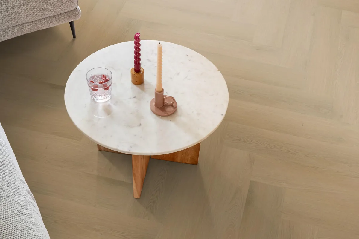 Merton / Navaro light oak, visgraat plak pvc in een woonkamer, met een ronde marmeren salontafel en twee kaarsen