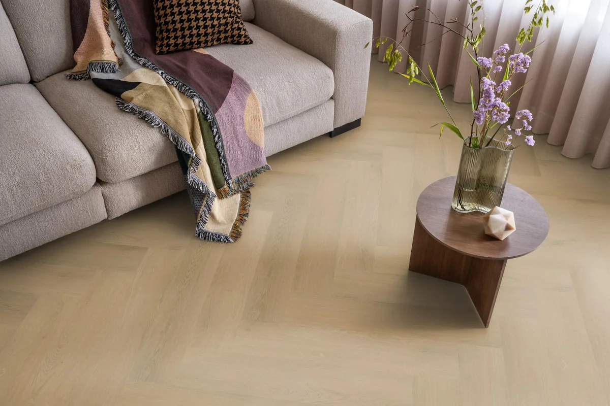 Merton / Navaro light oak, visgraat plak pvc in een woonkamer, met een beige bank en een ronde bijzettafel met bloemen