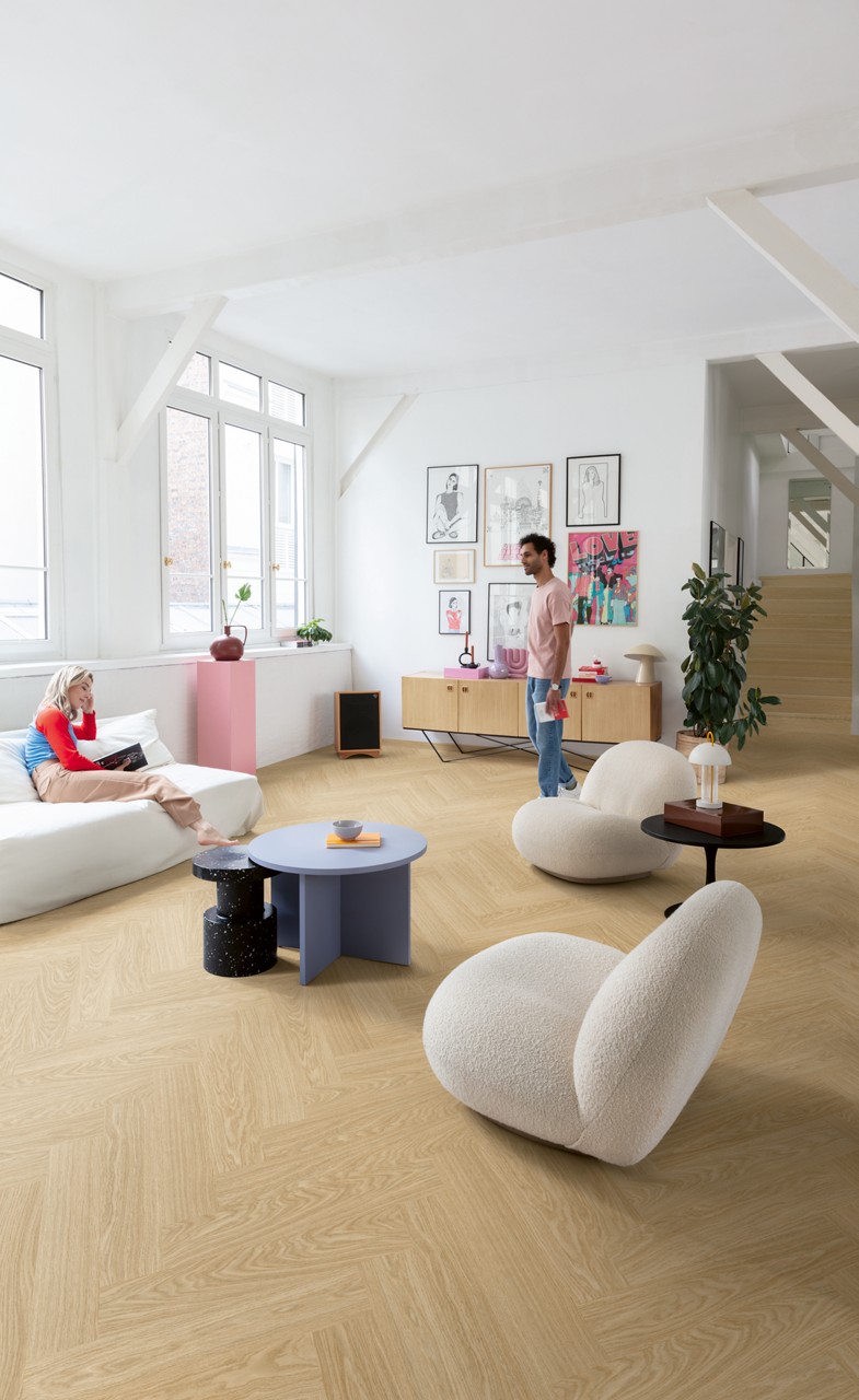Interieurfoto bij Quick-Step Pure eik blush AVHBU40359: visgraatvloer in een lichte woonkamer met een trap op de achtergrond.