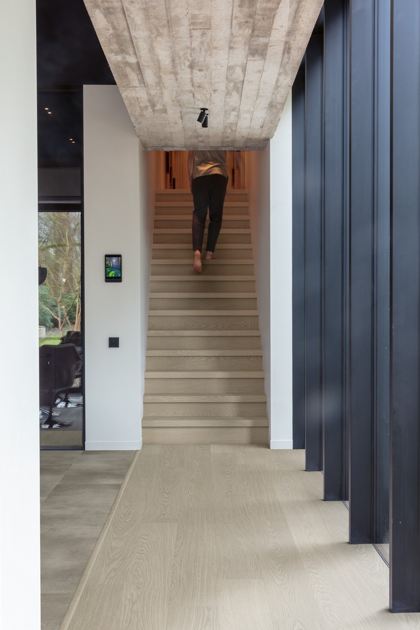 Interieurfoto bij Quick-Step Chia eik AVSPT40280: licht houtdecor op de vloer en trap naast een tegelvloer.