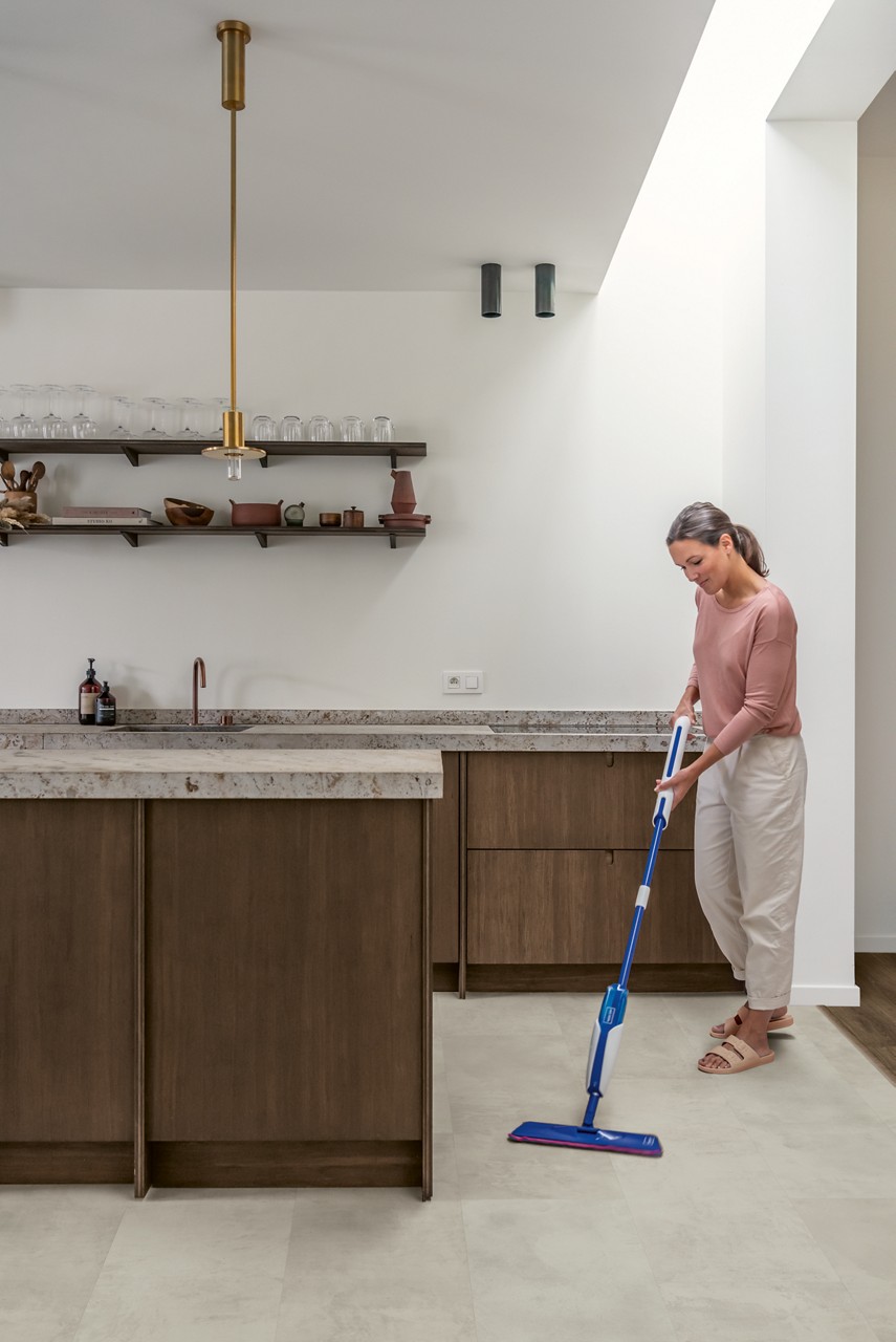 Interieurfoto bij Quick-Step Grijs beton MUS5488: grijze tegelvloer in een keuken tijdens het schoonmaken.