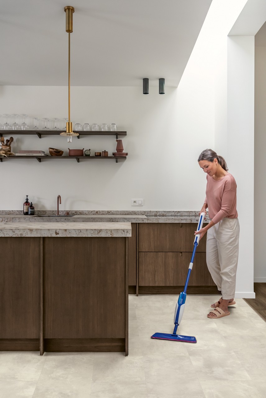 Interieurfoto bij Quick-Step Gevlekt beton MUS5491: lichte tegelvloer in een keuken tijdens het schoonmaken.